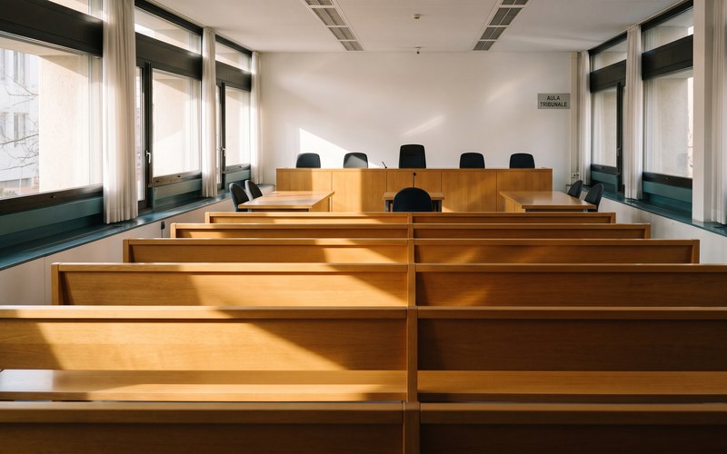 Tio.ch — Abusi sui minori, una sola risposta: tolleranza zero · Aula vuota del tribunale di Lugano con banchi in legno illuminati dalla luce naturale