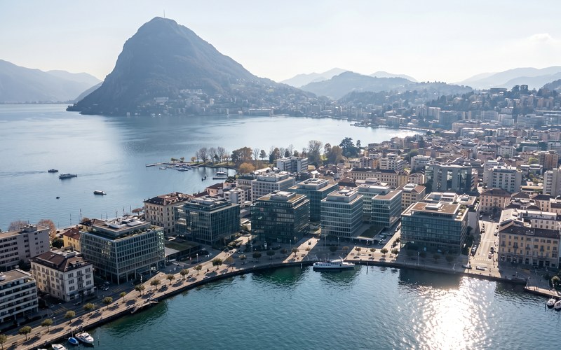 Tio.ch — Lugano, il nuovo rifugio strategico dei capitali globali · Vista aerea di Lugano-Paradiso con il Monte San Salvatore e il lago